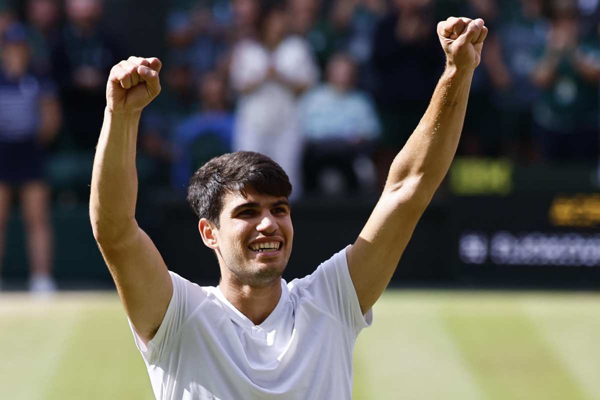 Carlos Alcaraz, vestito di bianco, esulta alzando i pugni al cielo dopo una vittoria a Wimbledon